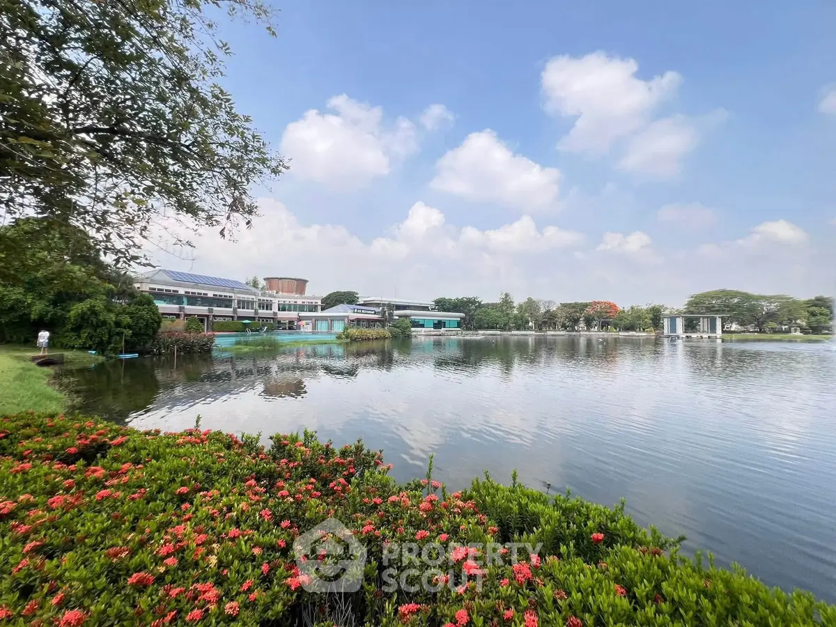 Scenic view of a serene lake with lush greenery and modern buildings in the background.