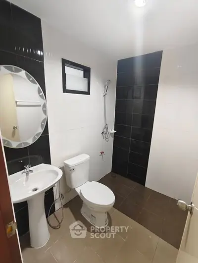 Modern bathroom with sleek black and white tiles, featuring a pedestal sink and shower area.