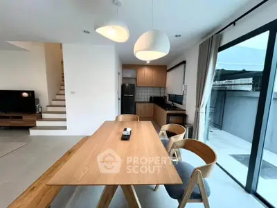 Modern dining area with wooden table and chairs, open kitchen layout, and large glass doors.