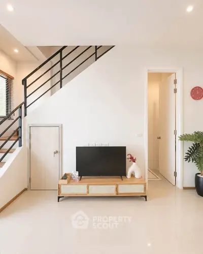 Modern living room with sleek staircase and stylish TV stand in a bright, open space.