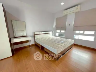 Spacious bedroom with wooden flooring and natural light, featuring a modern bed and air conditioning.
