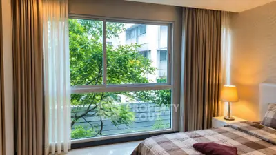 Cozy bedroom with large window offering lush green view, perfect for relaxation.
