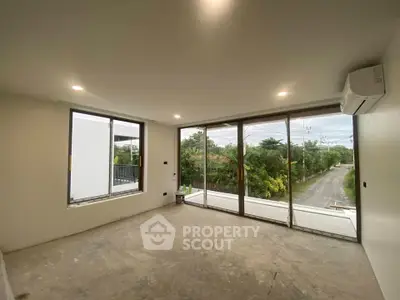 Spacious unfurnished room with large windows offering a scenic view of greenery and a quiet road.