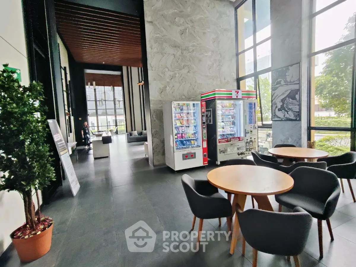 Modern building lobby with vending machines and seating area, featuring large windows and stylish decor.