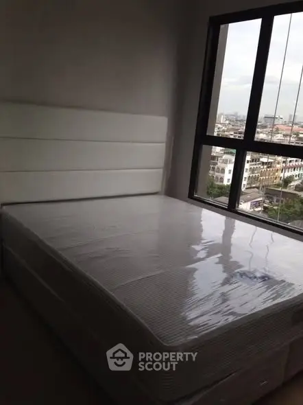 Cozy bedroom with large window offering city views, featuring a new mattress and modern headboard.