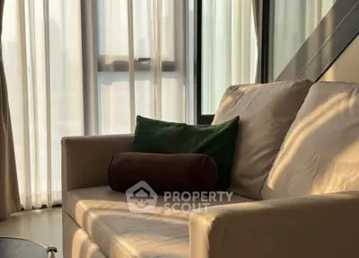 Cozy living room with elegant sofa and natural light through sheer curtains.
