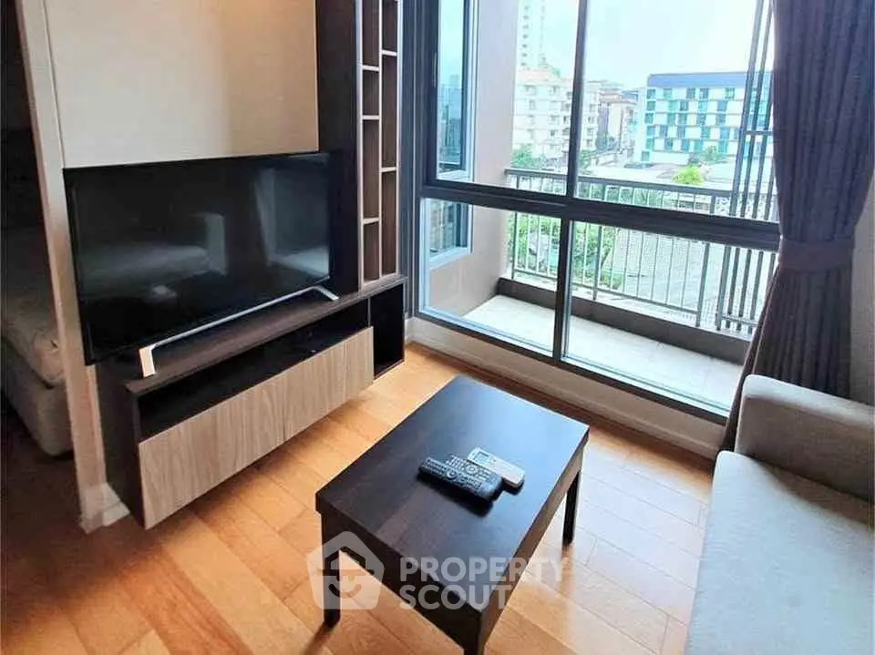 Modern living room with large window and city view, featuring sleek furniture and wooden flooring.