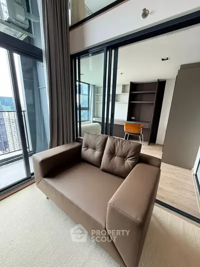 Modern living room with brown sofa and large windows offering city views, adjacent to a study area.