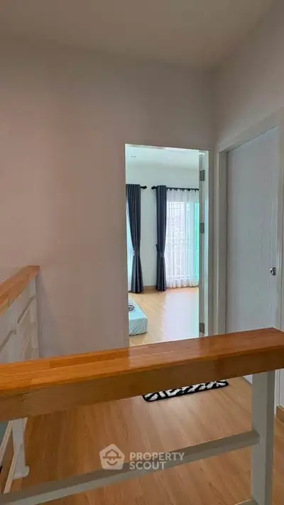 Bright hallway leading to a cozy bedroom with wooden flooring and elegant curtains.