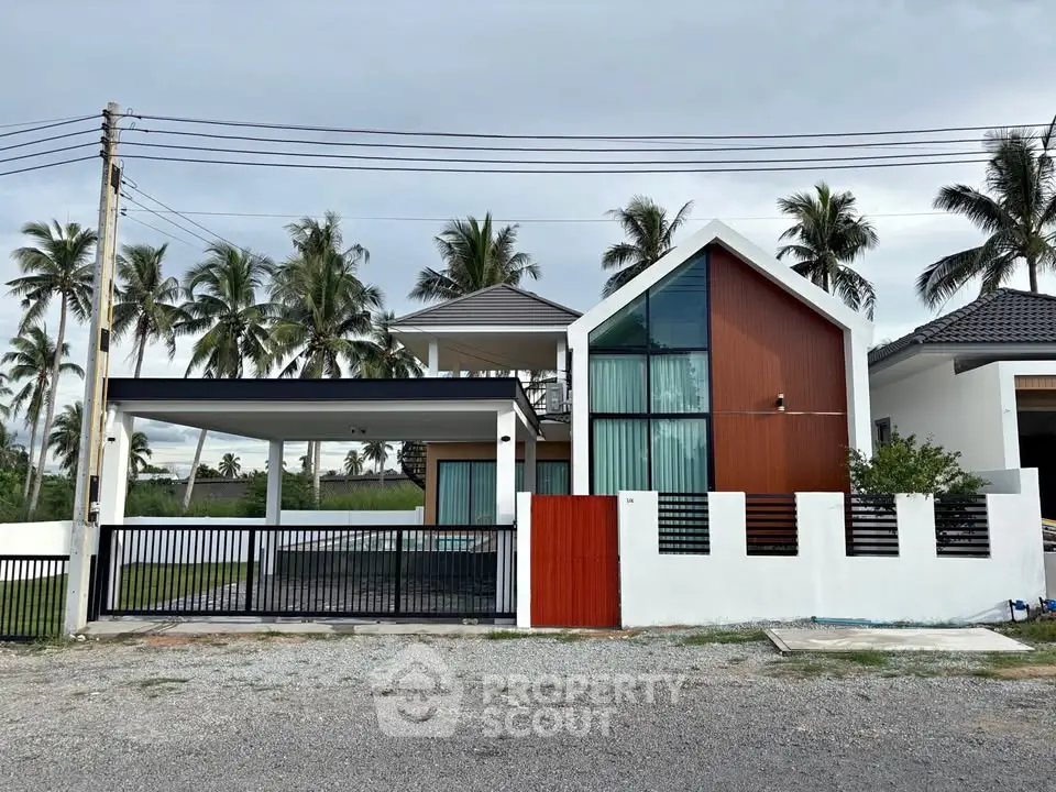 Modern two-story house with sleek design and large windows, surrounded by palm trees, offering a serene tropical setting.