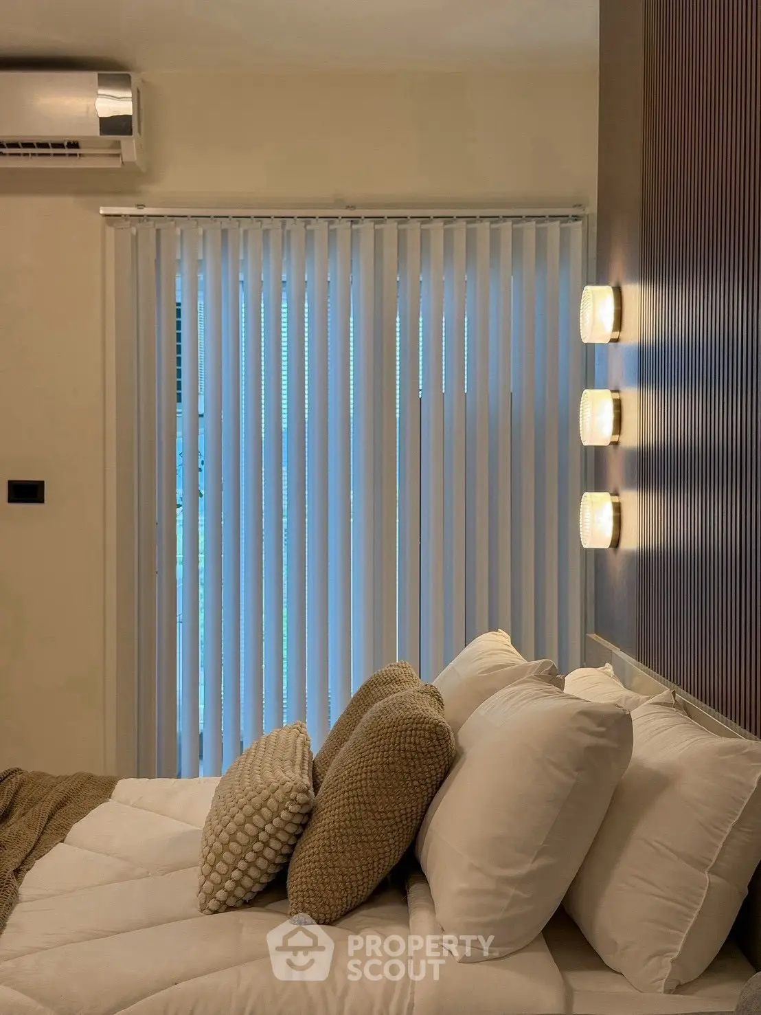 Cozy bedroom with modern lighting and air conditioning, featuring elegant vertical blinds and plush pillows.