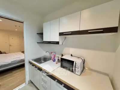 Modern kitchen with sleek cabinets and microwave, adjacent to cozy bedroom