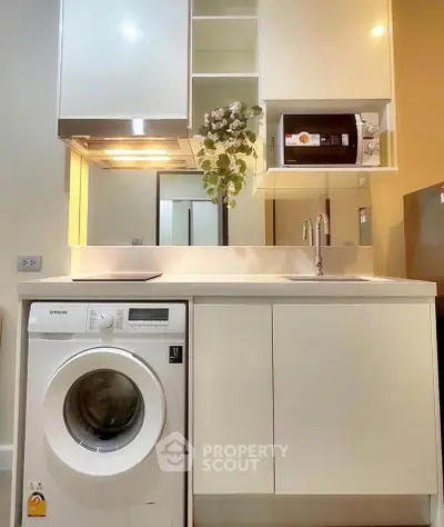 Modern kitchen with washing machine and microwave, sleek cabinetry and stylish design.