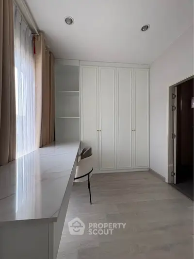 Modern study room with sleek white cabinetry and large window for natural light.