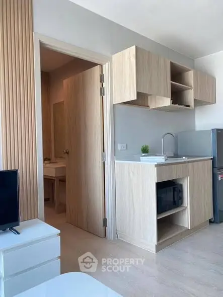 Modern compact kitchen with light wood cabinets and open shelving in a stylish apartment.