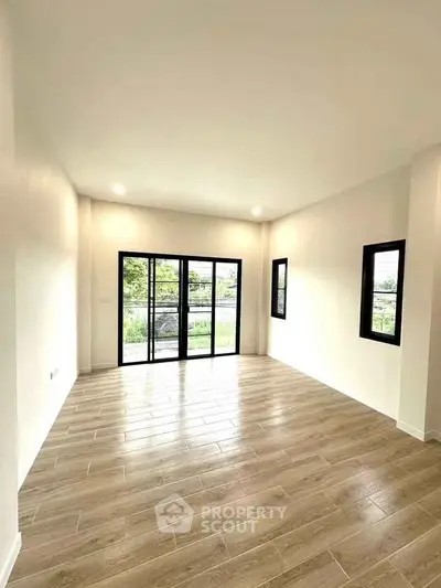 Spacious modern living room with large windows and wooden flooring, offering abundant natural light.