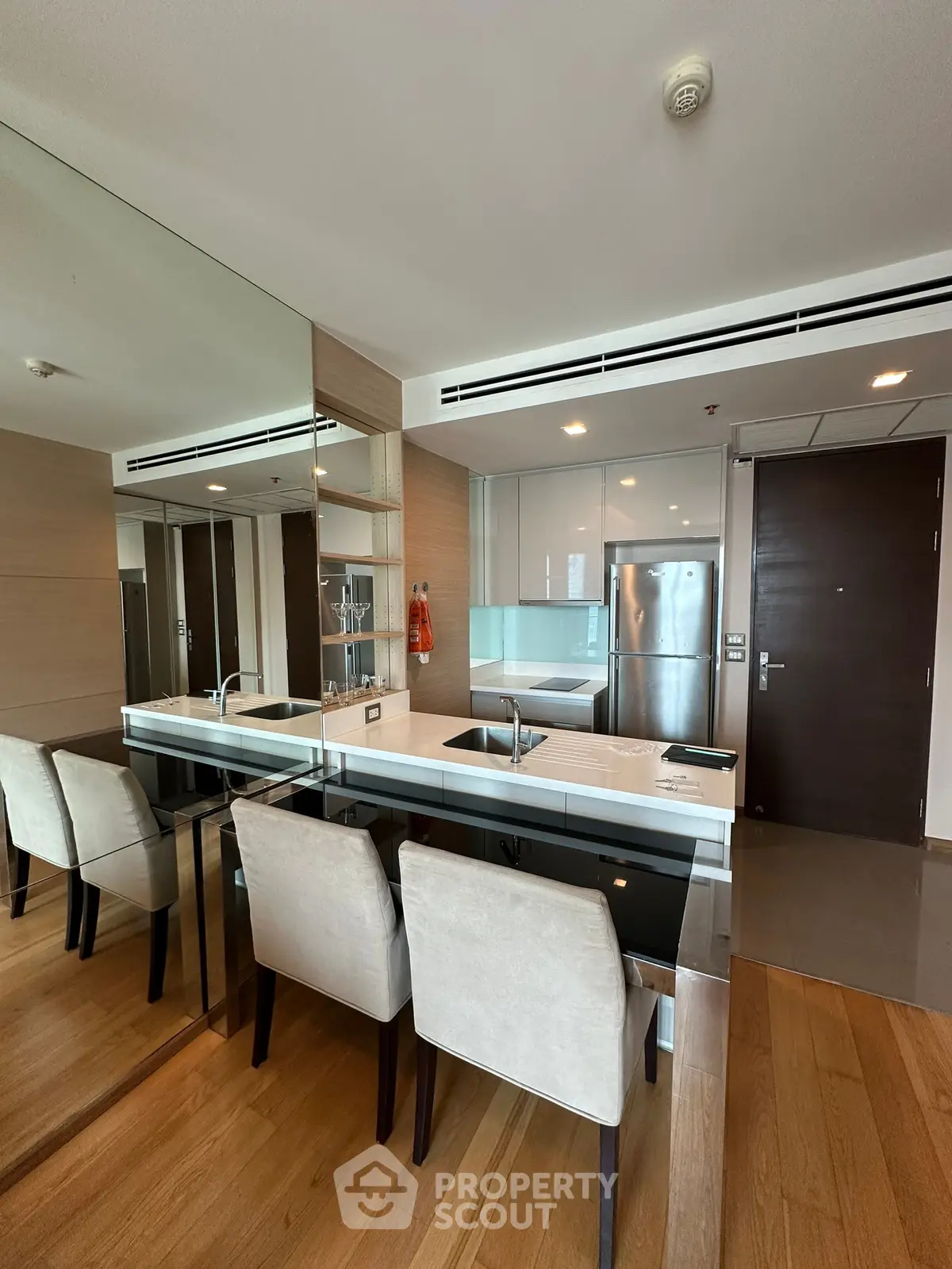 Modern kitchen with sleek design and mirrored wall, featuring stainless steel appliances and elegant dining area.