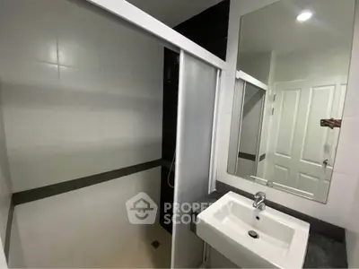Modern bathroom with sleek sink and mirror, featuring a sliding shower door.