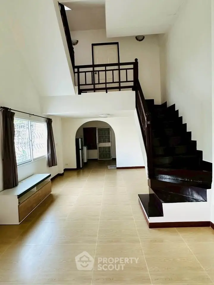Spacious two-story living room with elegant staircase and large window for natural light.