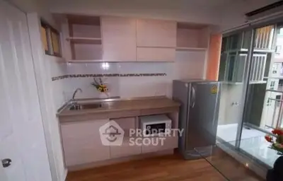 Compact modern kitchen with fridge and microwave, featuring sleek cabinetry and balcony access.