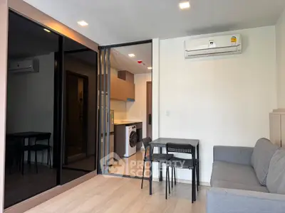 Modern living room with open kitchen, featuring sleek design and air conditioning.