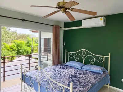 Spacious bedroom with elegant bed, ceiling fan, and lush green view from balcony.