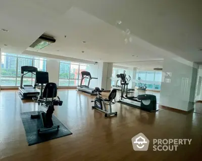 Spacious gym with modern fitness equipment and city view in luxury apartment building.