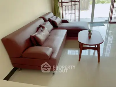 Modern living room with stylish brown leather sofa and wooden coffee table near large window.