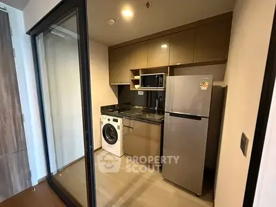 Modern compact kitchen with appliances including fridge, microwave, and washing machine in sleek apartment.