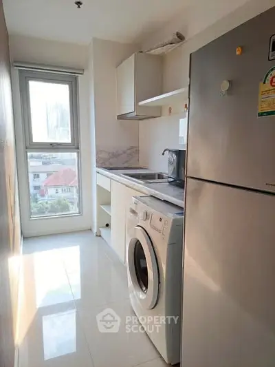 Modern kitchen with washing machine and fridge, featuring sleek cabinetry and a bright window view.