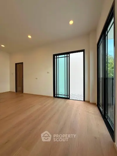Spacious empty room with wooden flooring and large windows offering natural light.