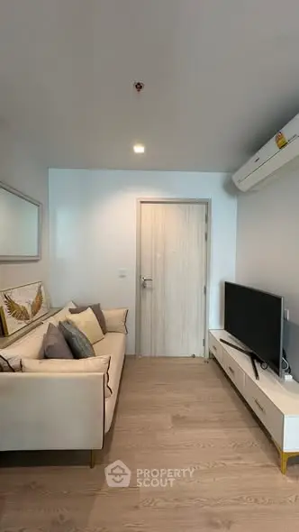 Modern living room with cozy sofa and flat-screen TV, featuring sleek wooden flooring and minimalist decor.