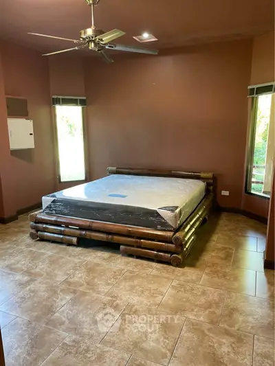 Spacious bedroom with bamboo bed frame and ceiling fan, featuring large windows and tiled flooring.