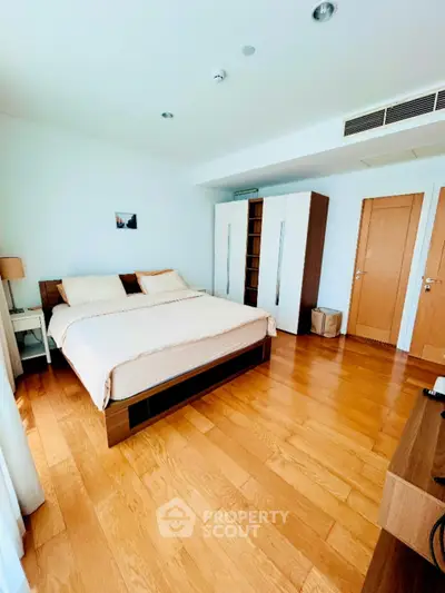 Spacious bedroom with wooden flooring and modern furniture in a bright apartment.