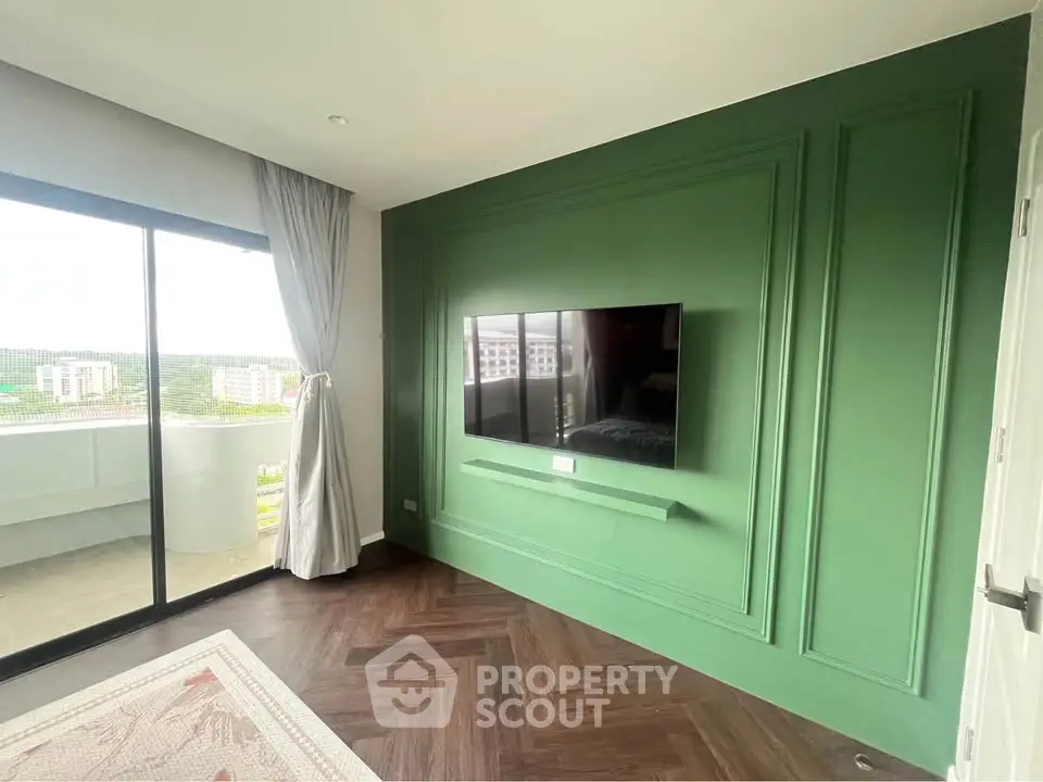 Modern living room with green accent wall and large TV, featuring a balcony with city view.
