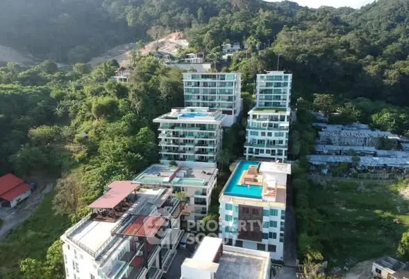 Aerial view of modern apartment buildings surrounded by lush greenery and hills.