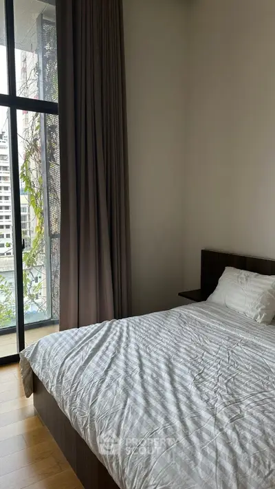 Modern bedroom with large window and city view, featuring a cozy bed and elegant curtains.