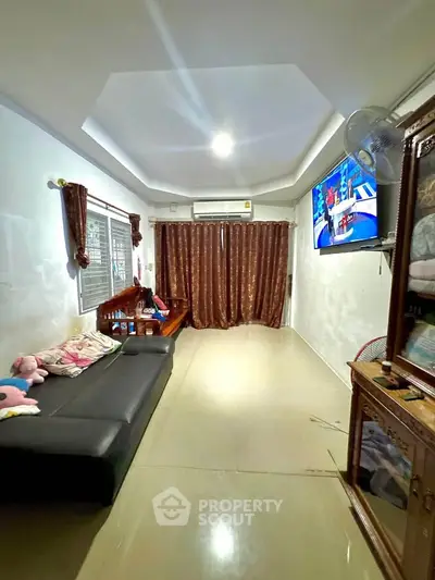 Spacious living room with modern decor and natural light, featuring a comfortable sofa and wall-mounted TV.