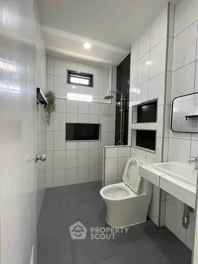 Modern bathroom with sleek tiles and contemporary fixtures, featuring a shower and toilet.