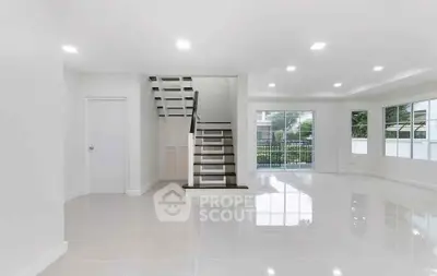 Spacious modern living room with glossy floors and staircase, abundant natural light, and garden view.