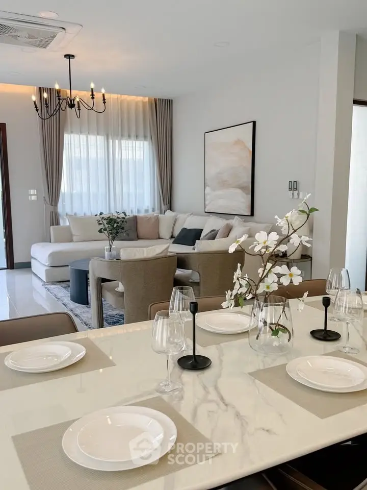 Elegant living room with modern decor and dining area, featuring a cozy sofa and stylish chandelier.