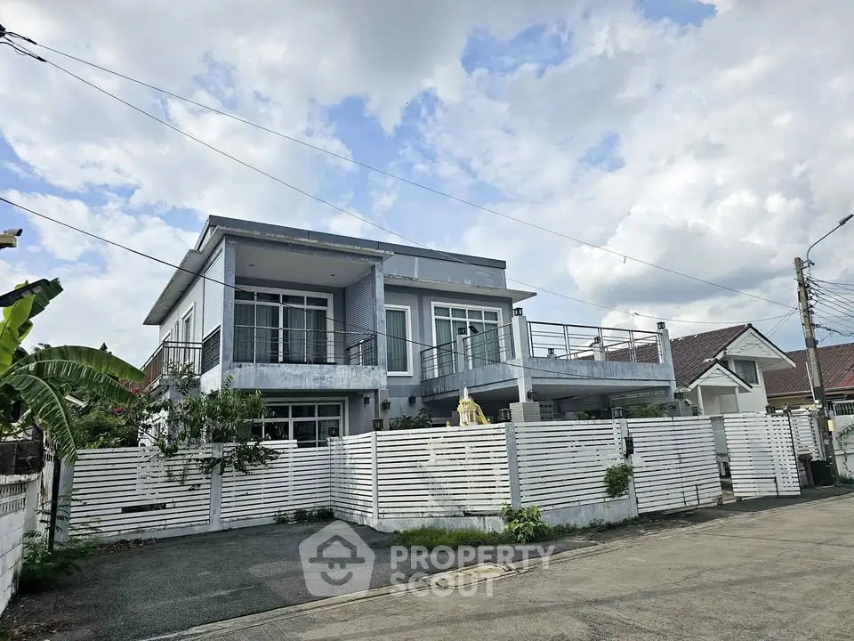 Modern two-story house with spacious balcony and white fence under a blue sky.