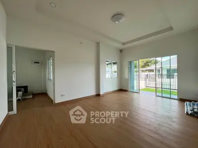 Spacious empty living room with wooden flooring and large windows opening to a garden view.