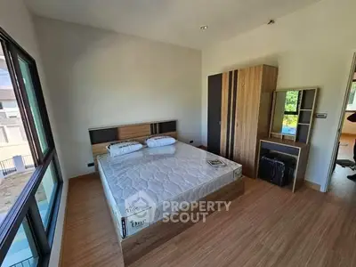 Modern bedroom with large window and wooden flooring, featuring a bed and wardrobe.