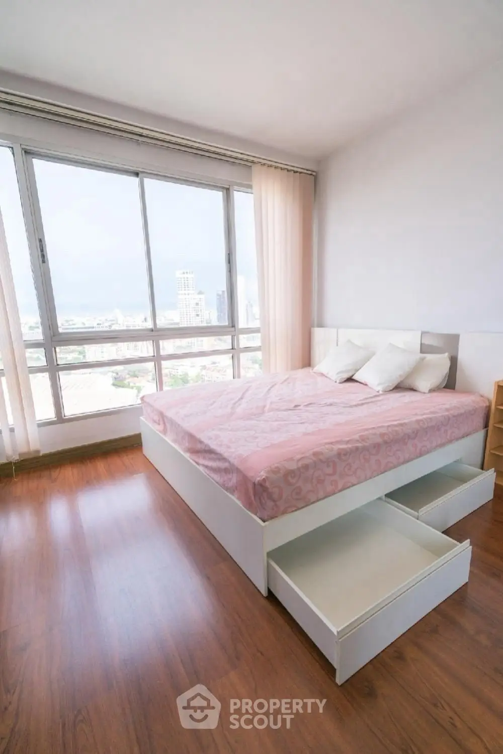 Spacious bedroom with large windows offering a stunning city view, featuring a modern bed with storage drawers.