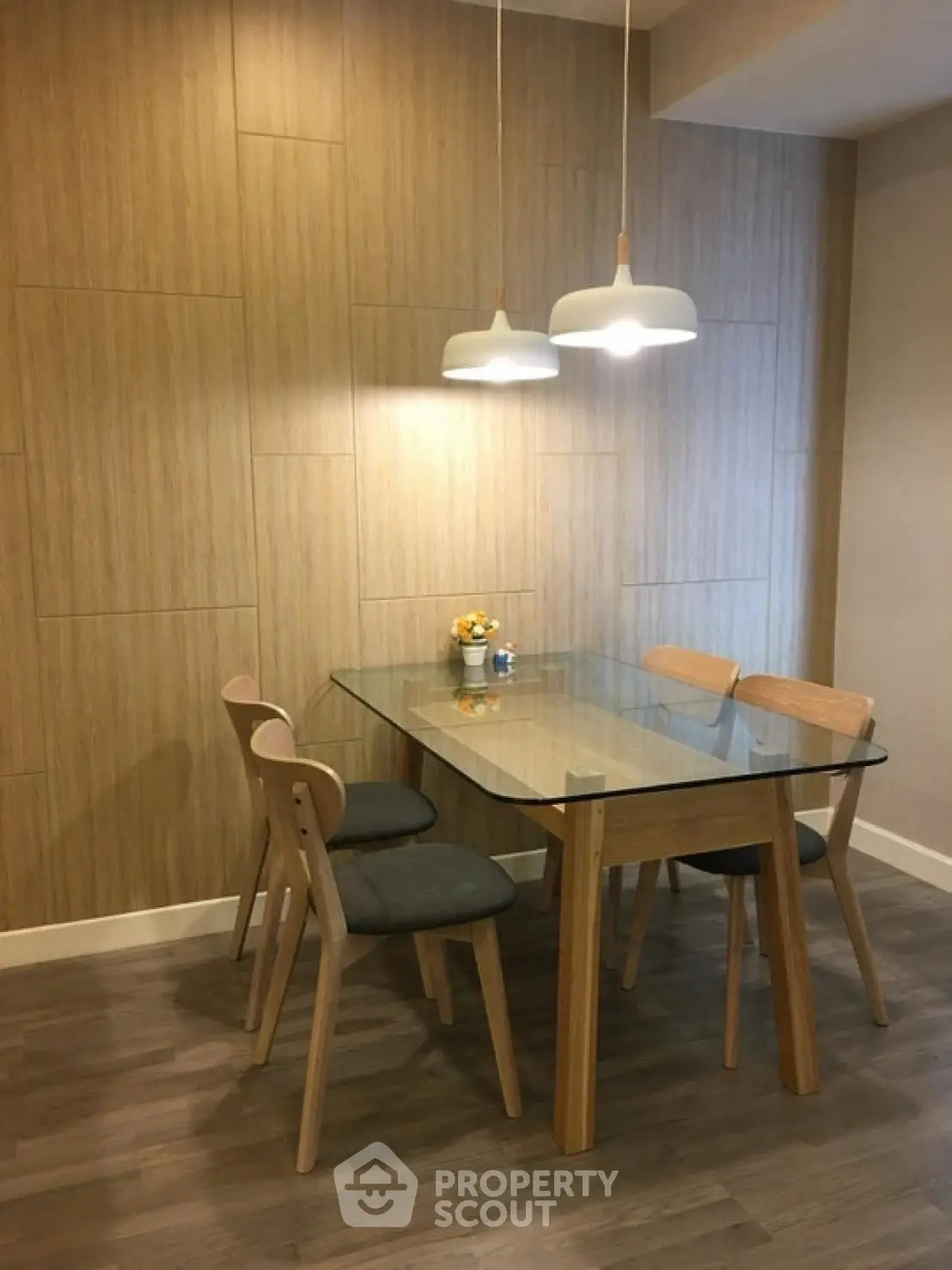 Modern dining area with glass table and wooden chairs, featuring stylish pendant lighting.