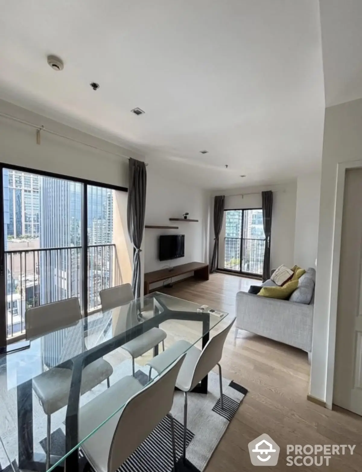 Modern living room with glass dining table and city view, spacious and bright interior.