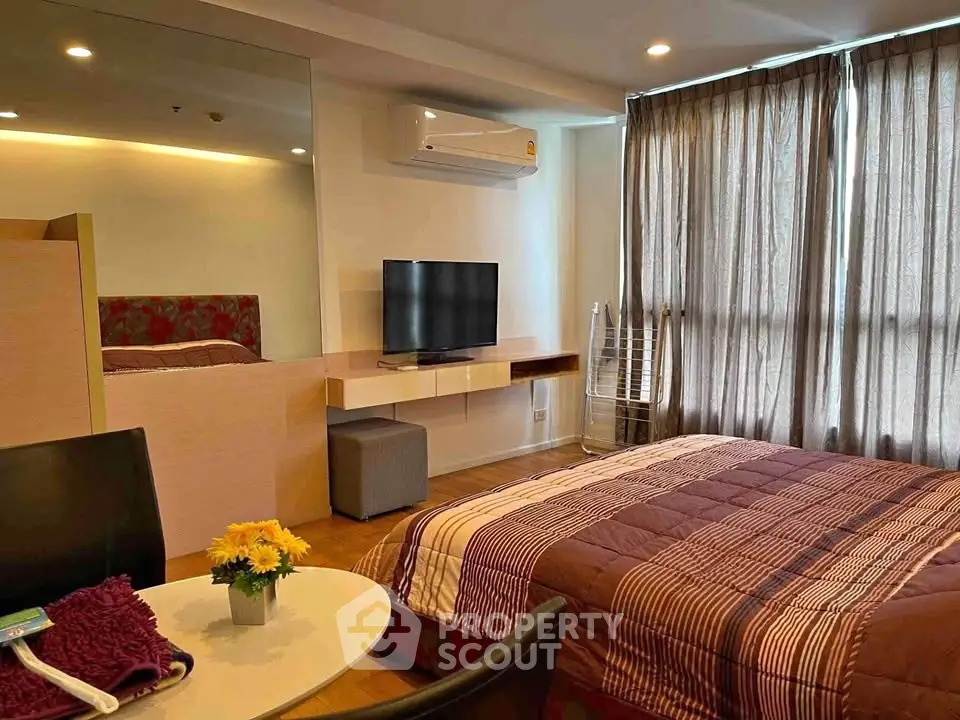 Cozy bedroom with modern decor, featuring a wall-mounted TV and large window with curtains.