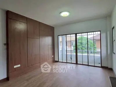 Spacious empty room with wooden flooring and large windows leading to balcony.