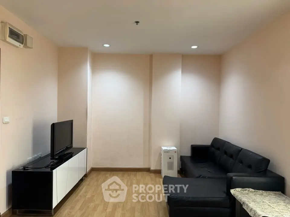 Cozy living room with modern black sofa and flat-screen TV, perfect for relaxation.